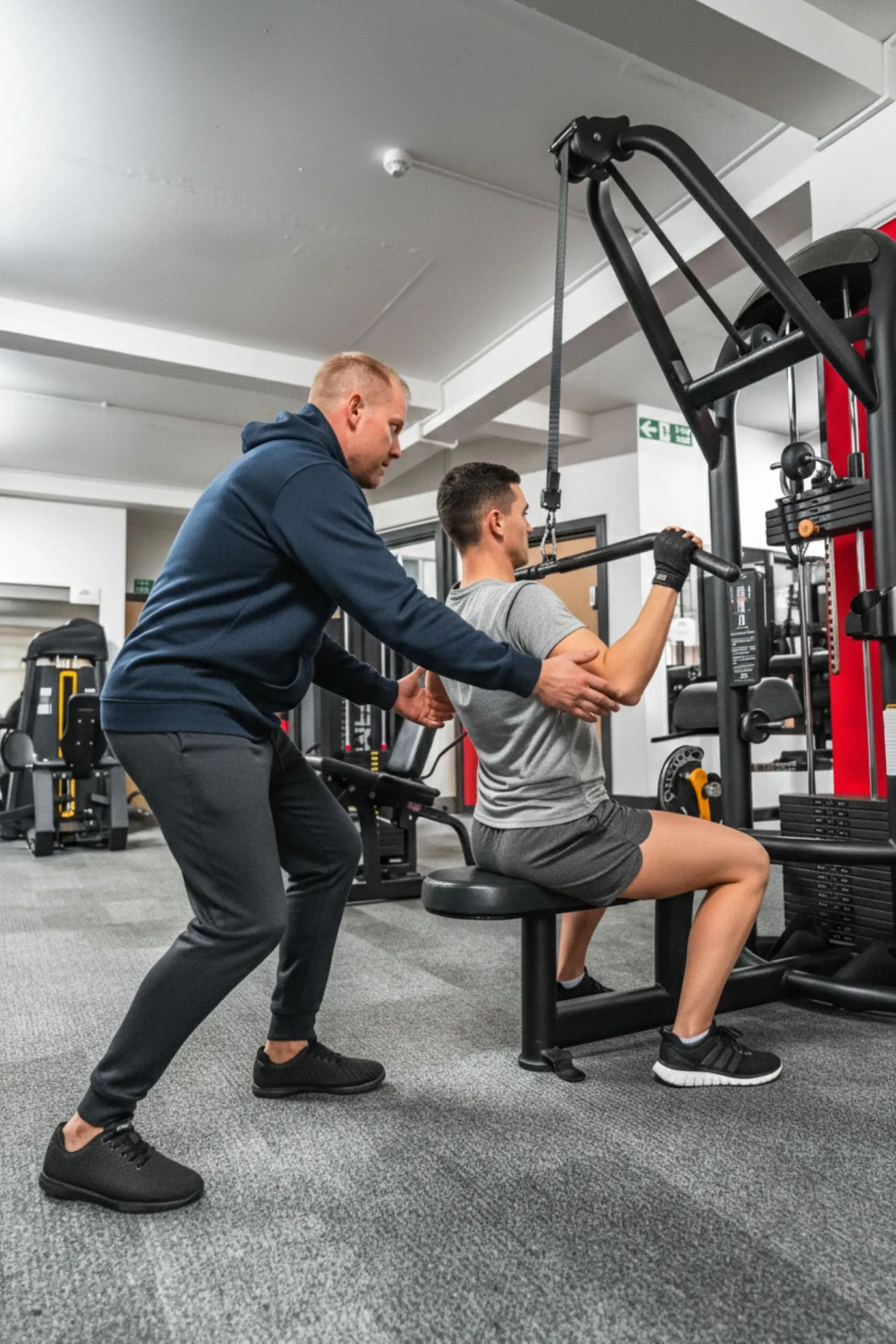 Personal trainer eşliğinde spor aletinde antrenman yapan danışan