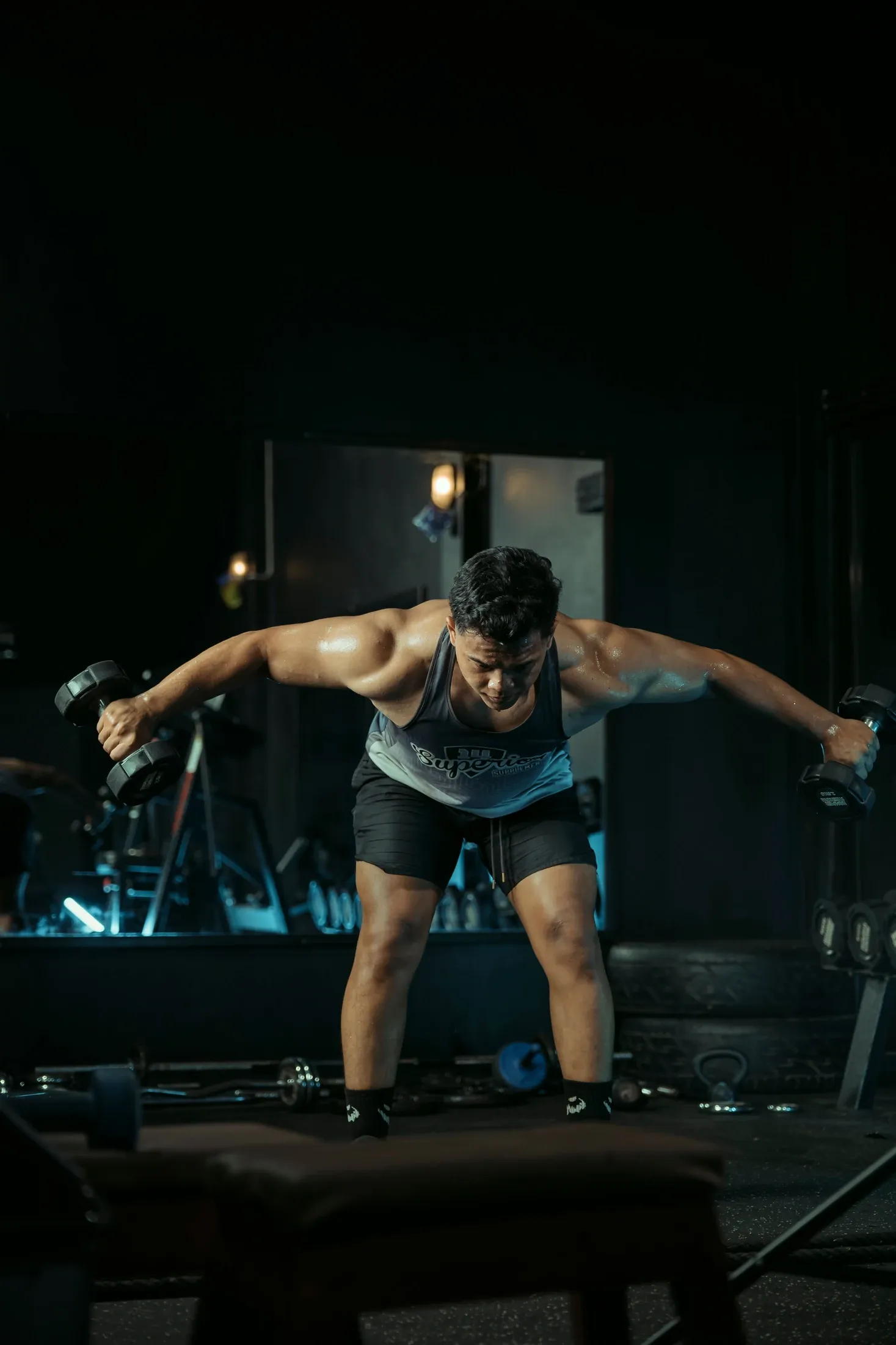 Karanlık spor salonunda dambıllarla kuvvet antrenmanı yapan sporcu